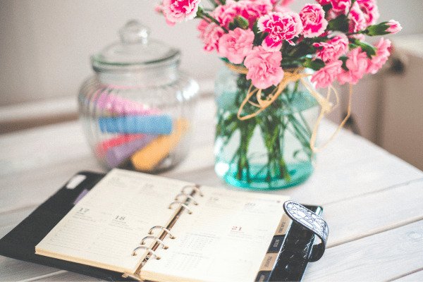 Como criar um sistema de organização pessoal que realmente funciona-mesa com vaso de flores rosas agenda aberta e pote de vidro com coisas coloridas dentro.jpg