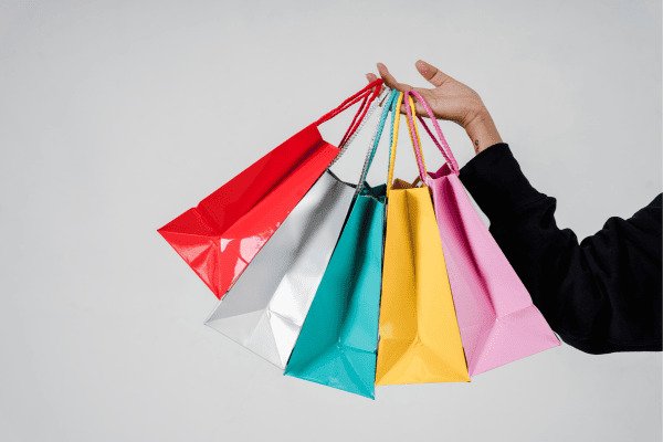 Mãos segurando sacolas de papel coloridas - Compras conscientes o guia minimalista para gastar menos e viver melhor
